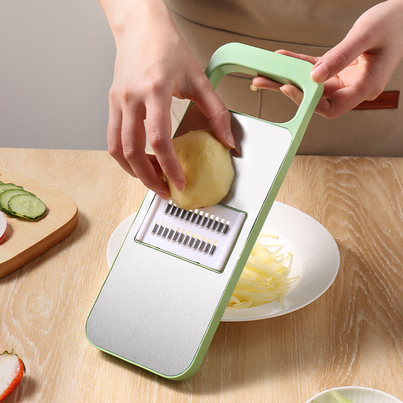 Person using a green vegetable slicer to cut a potato on a wooden table.