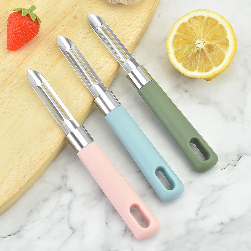 Three vegetable peelers with colorful handles on a marble surface with a lemon and strawberry.