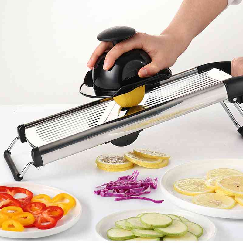 Person using a mandoline slicer to slice lemons on a white surface with sliced vegetables displayed.